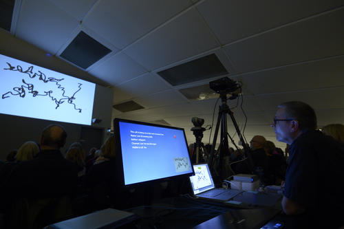 Skripturale Methode: Alex Malik zeichnet Kringel, Kurven und Linien, die über einen Beamer an die Wand geworfen werden.