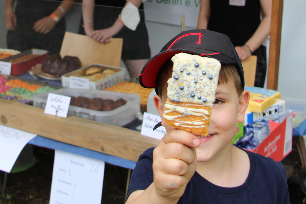 Ein Junge mit Mütze hält einen Kuchen-Lolli, der mit Guss und Perlen verziert ist