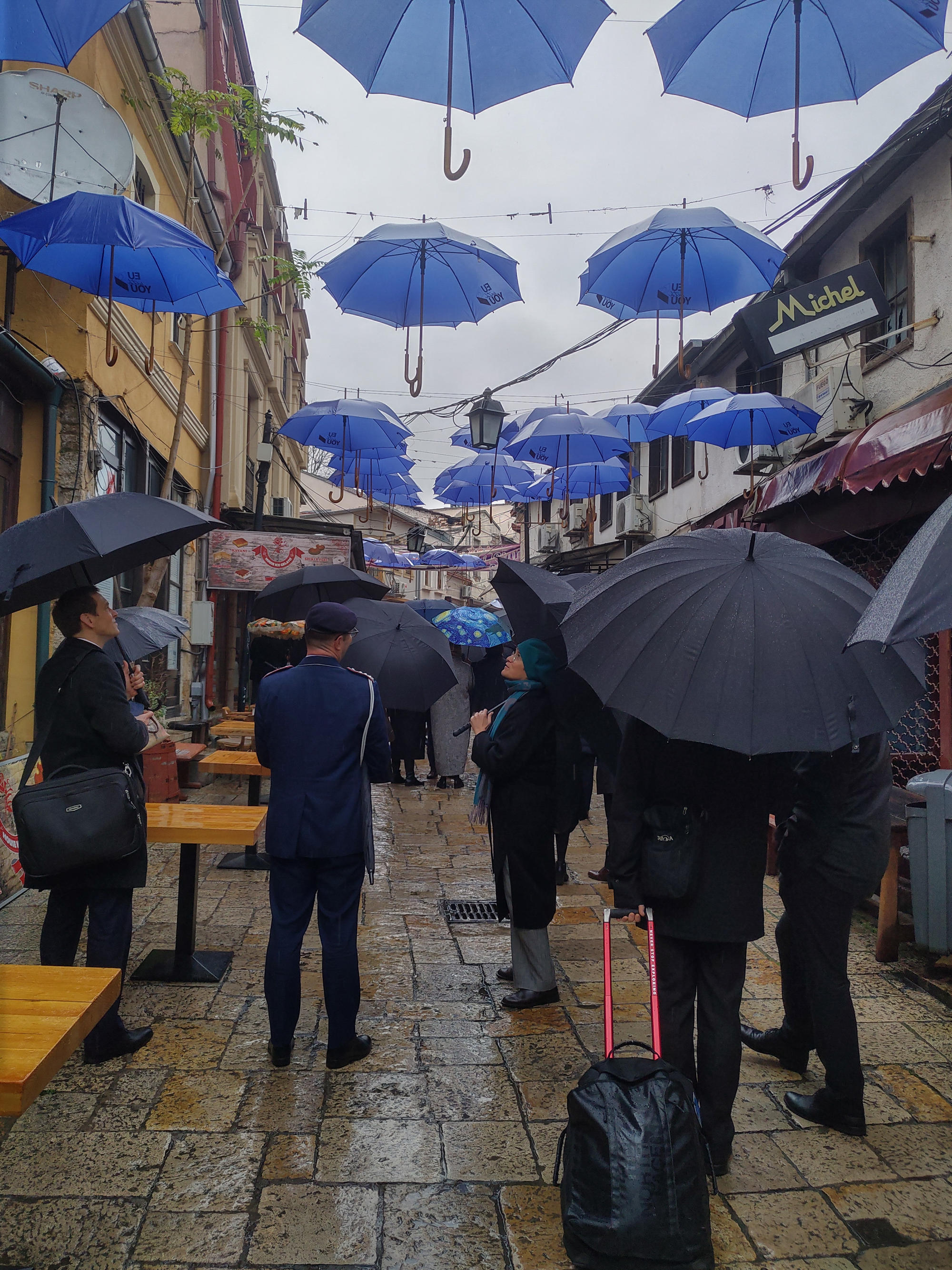 A rainy walk through the old town of Skopje, under a sky formed by EU umbrellas.