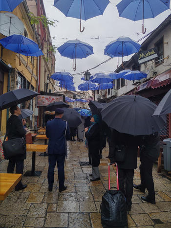 A rainy walk through the old town of Skopje, under a sky formed by EU umbrellas.