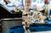 Dieses schmucke Stück aus hitzebeständigem Borosilikatglas ist der Rest eines dicken Glasrohrs. Ein schmales Rohr wird daran angeschmolzen, damit sich das Material optimal nutzen lässt, ohne die Spannbacken der Drehbank durch Hitze zu beschädigen.