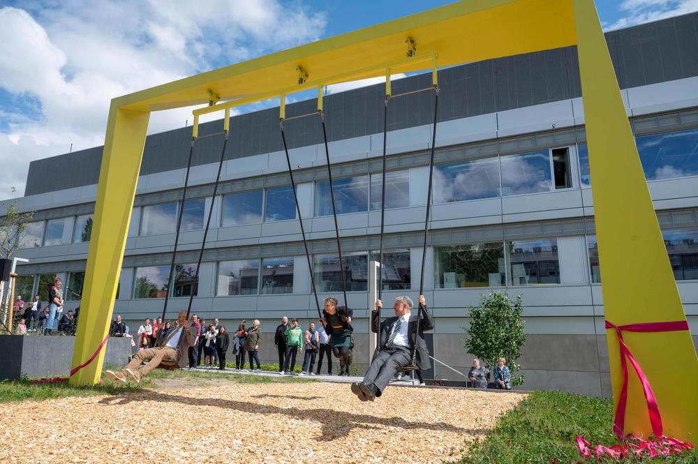 Prof. Rainer Haag, Prof. Stefanie Reich und Peter Lange schaukeln auf der SupraSwing-Schaukel neben dem Forschungsgebäude SupraFAB.